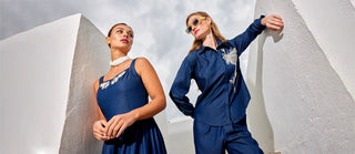 Two women in blue outfits posing against a white architectural background