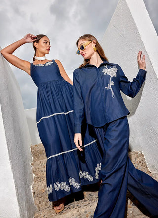 Two women in navy blue outfits with white floral embroidery standing against a textured wall.