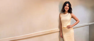 Woman in a light-colored dress standing against a plain wall.