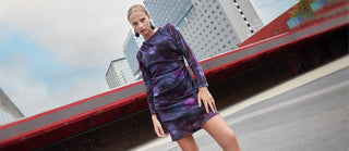 Woman in a purple dress standing on a street with buildings in the background