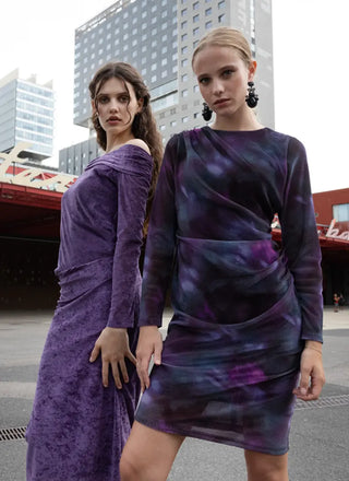 Two women wearing purple dresses standing in an urban setting.