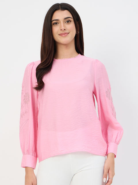 Woman wearing a pink blouse with floral embroidery on a light gray background