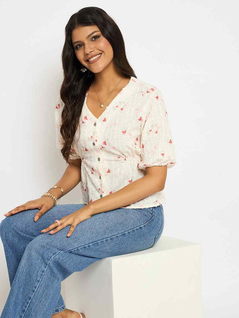 Woman wearing a white floral blouse and blue jeans sitting on a white surface with a white background