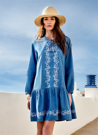 Woman wearing a blue dress with white embroidery and a straw hat against a blue sky.