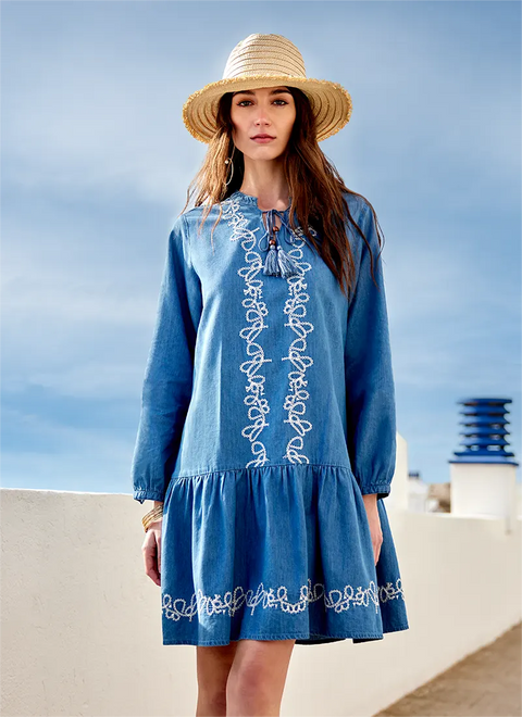 Woman wearing a blue dress with white embroidery and a straw hat against a blue sky.
