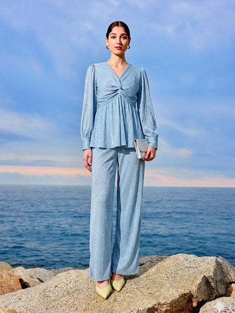 Woman in a light blue outfit standing on rocks with ocean and sky in the background
