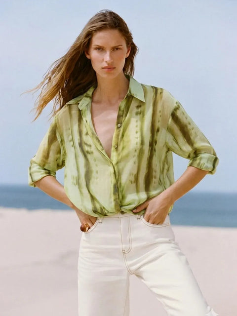 Woman wearing a green patterned shirt and white pants on a beach.